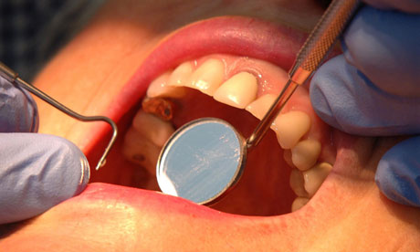 A dentist examines a patient's teeth with a mirror